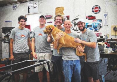 The five guys in the shop with one holding a dog.