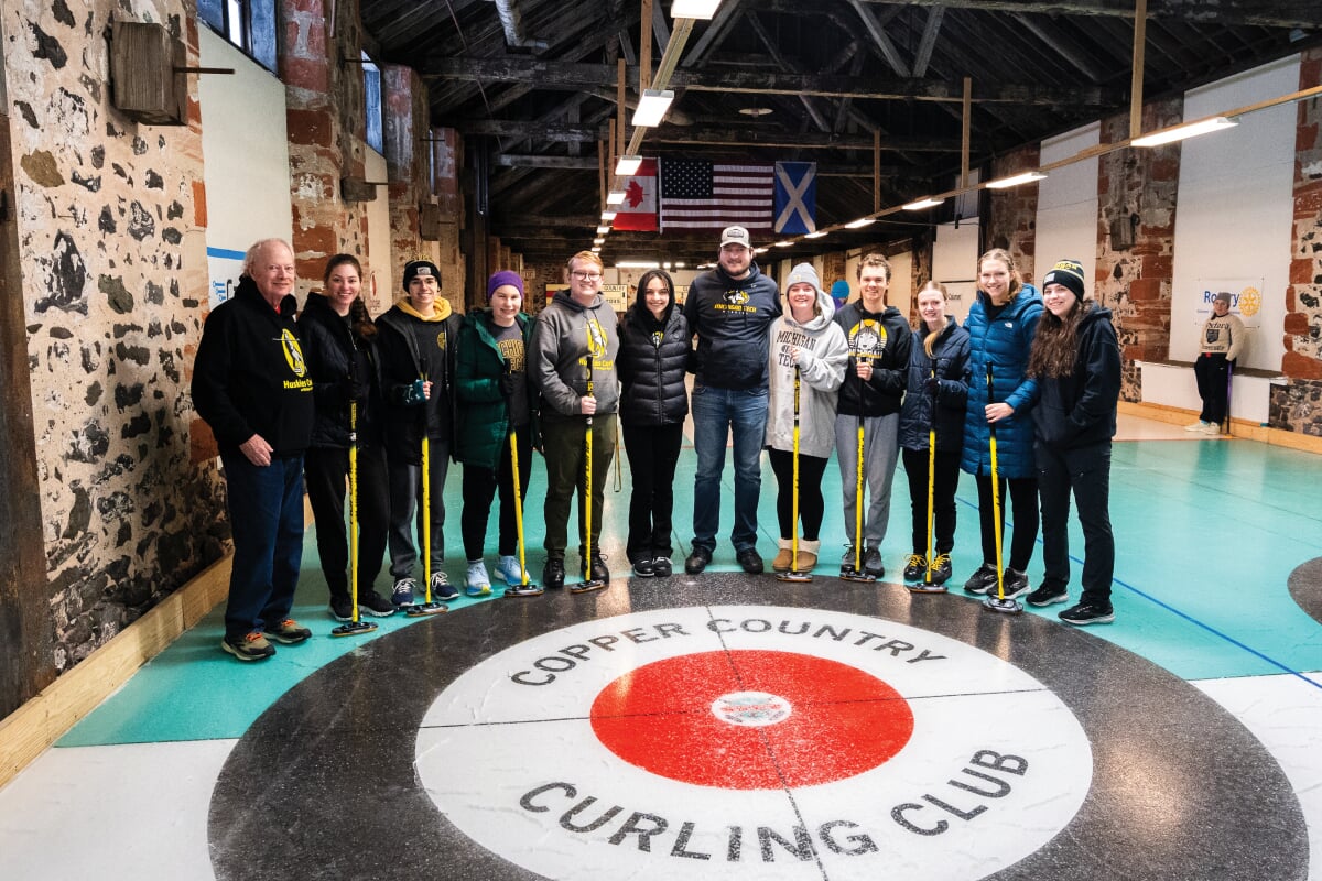 Curling Club stands in a line holding their brooms.