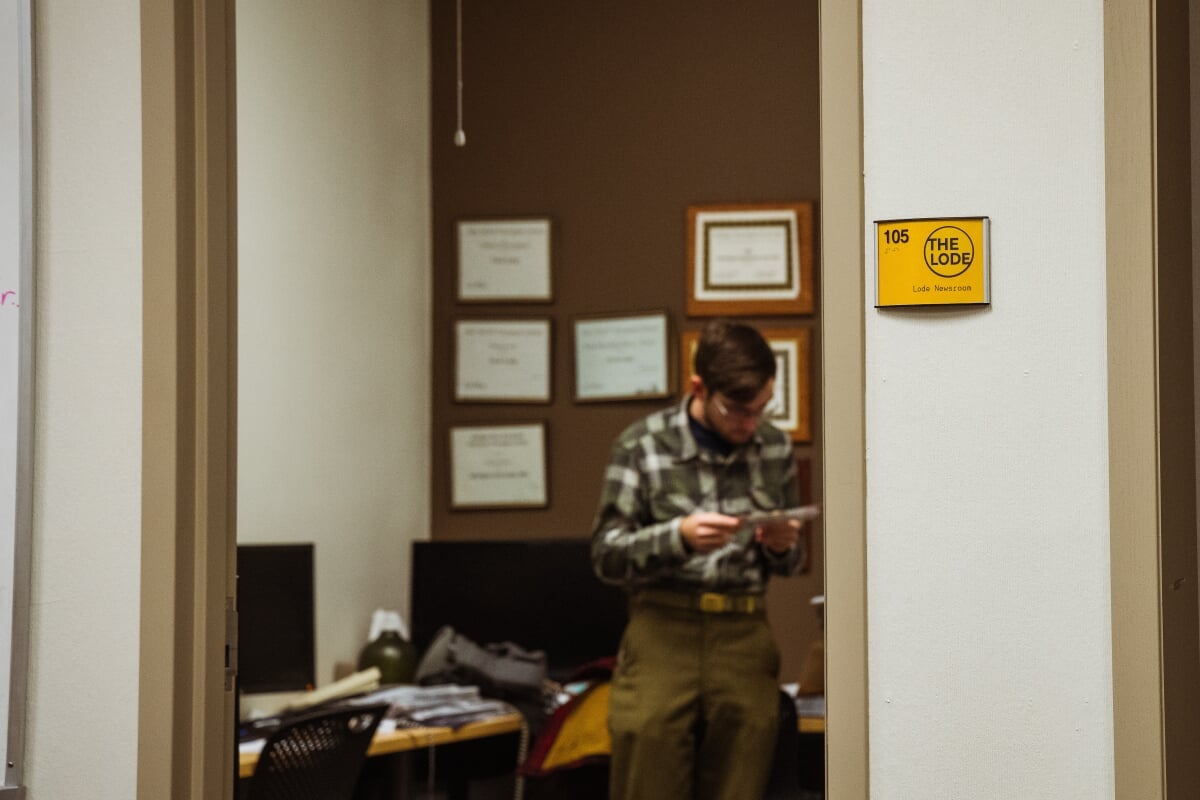 Student standing in an office with a sign outside the doorway reading "106 The Lode"