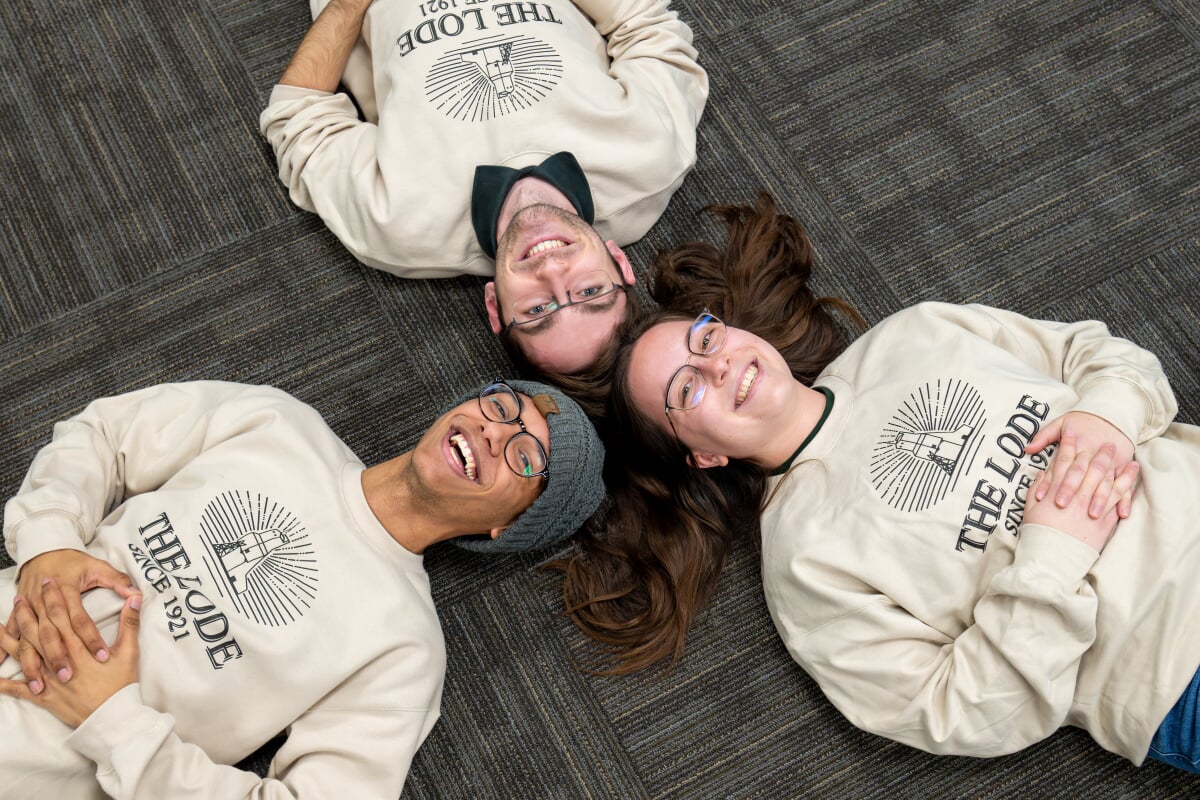 Three students wearing The Lode sweatshirts laying on the floor.