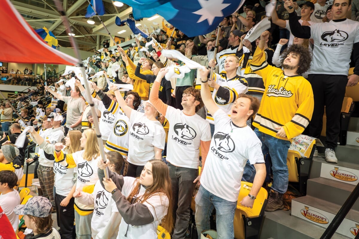 Group of students wearing Michigan Tech apparel cheering in the stands.