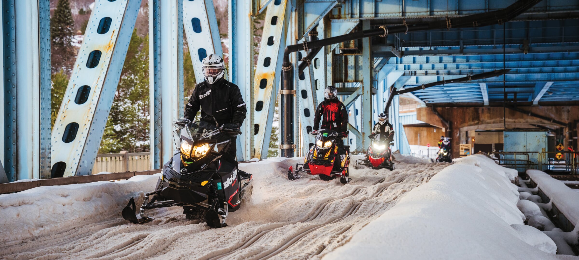 Four snowmobiles riding on the trail under the Portage Lake Lift Bridge.