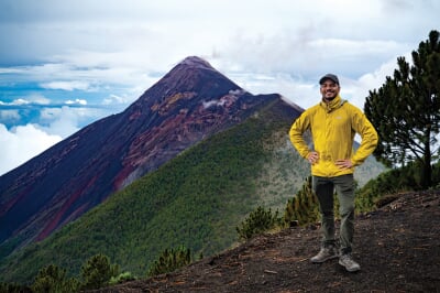 Gustavo Bejar-Lopez standing on a mountain with a smoking volcano in the background.