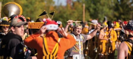 Cue the Pep! Third-year electrical engineering student and snare drummer Ben Paddock raises his drumsticks in glowing golden-hour sunshine, surrounded by fellow Huskies Pep Band members kitted out in their black and gold stripes and Husky Spirit attire. In the background, the leaves are beginning to turn that renowned Keweenaw orangeâ€”and with temperatures still warm enough for short sleeves? Weâ€™d be smiling, too!