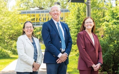 Three new deans standing outside in front of the Rekhi to Library bridge.