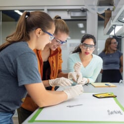 Two students working on an experiment while a professor supervises.