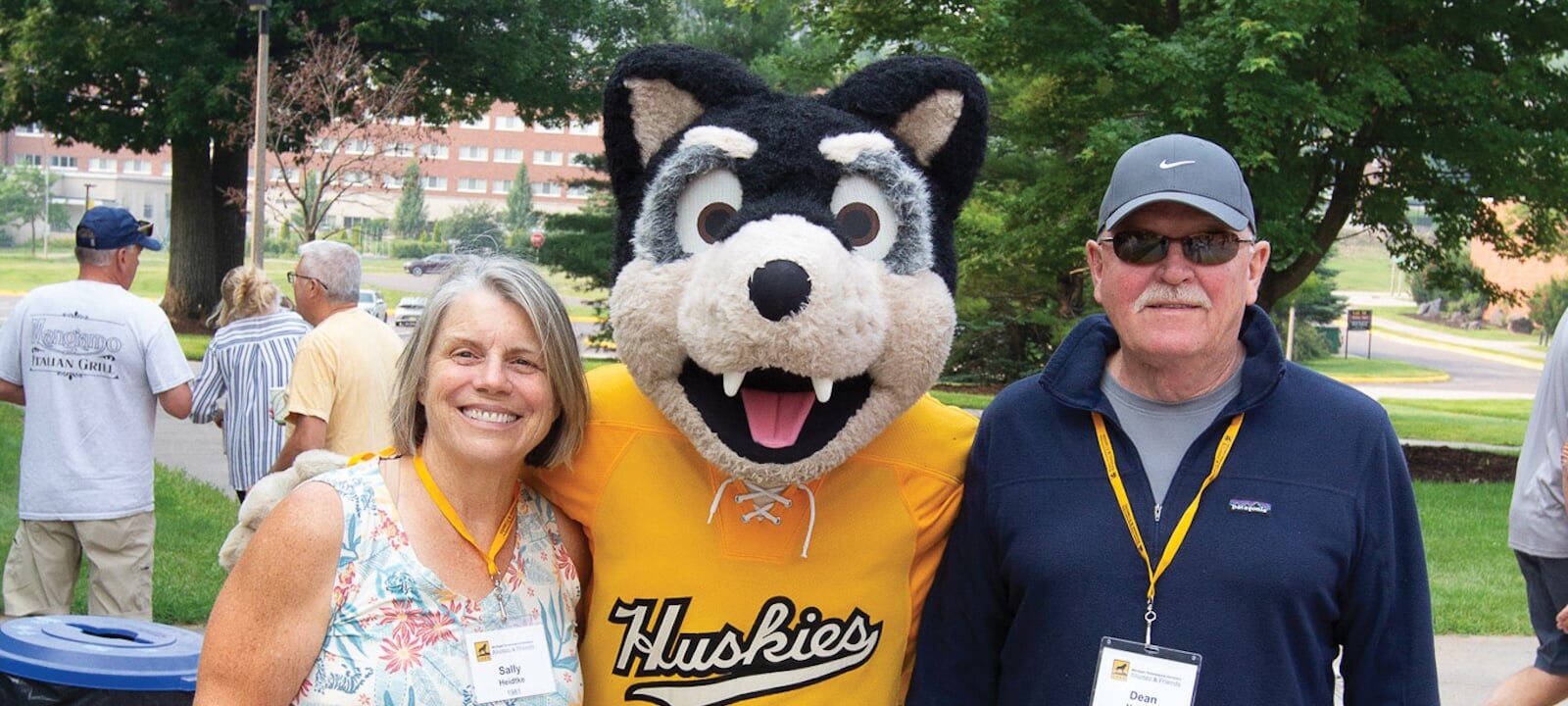 Blizzard T. Husky standing between two alumni reunion attendees.