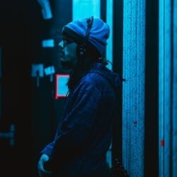 Stage crew member wearing a headset, standing in the wings in the dark.