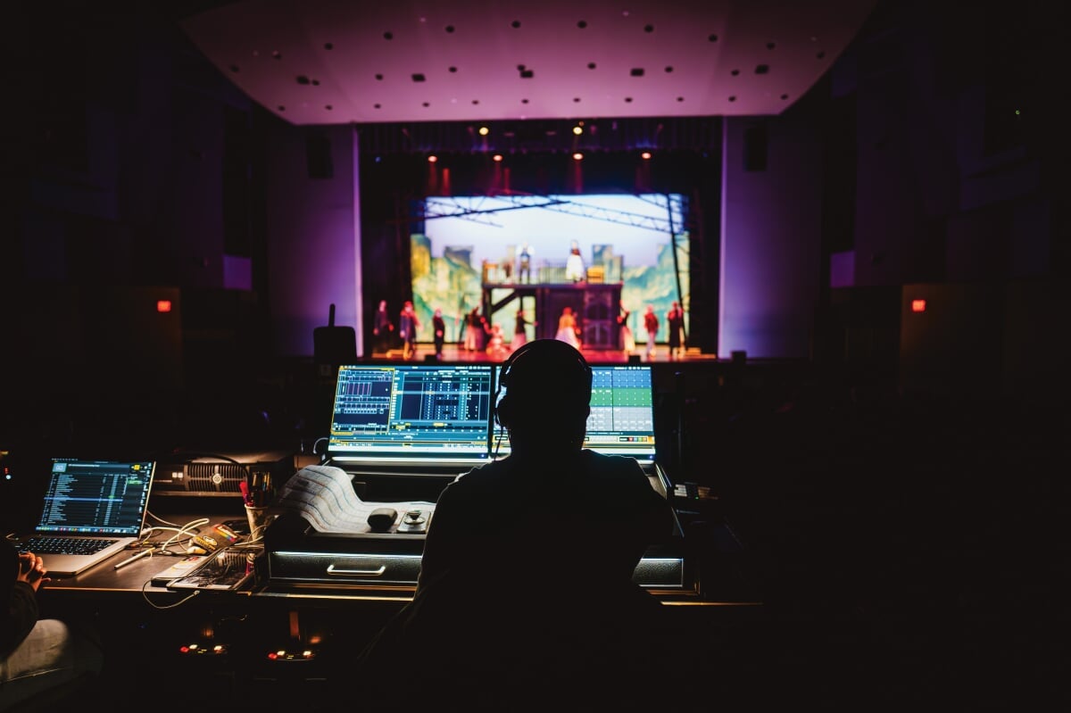 Person sitting at the sound and lighting board during a performance.