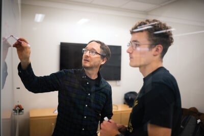Paul Goetsch writing on a whiteboard while a student looks on.