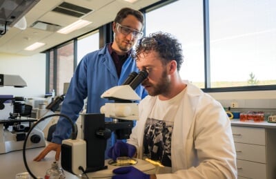 Paul Goetsch watches as a student looks at a sample under a microscope.