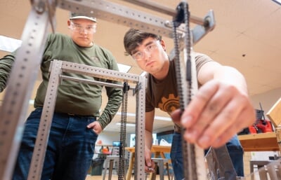 Two students fitting a chain on a robot.