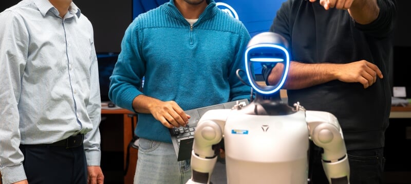 Three people standing behind a humanoid-looking robot.