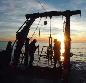 The team works with a multi-corer that uses gravity and spring-loaded cylinders to extract cores of mud from the lake bottom.