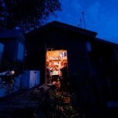 A man and two women stand in a lit-up cabin at dawn.