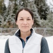 A woman in a white vest has her dark hair pulled back.