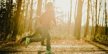 Two children running on a dirt path in the woods.