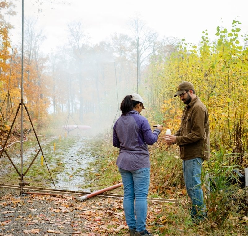 Two researchers next to a forest road with machines spraying water.