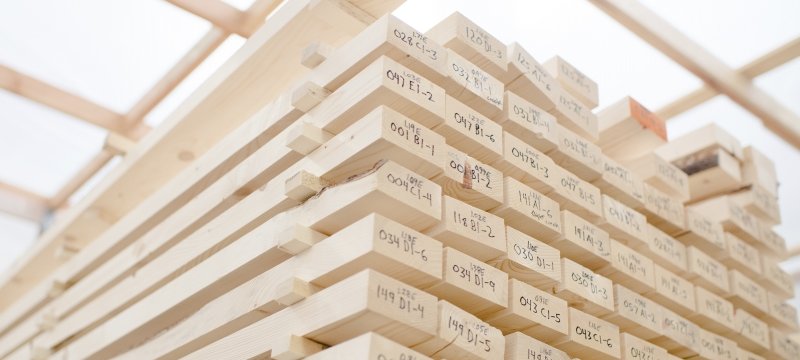 A stack of two-by-four lumber is arranged neatly with handwritten marks on the short ends.