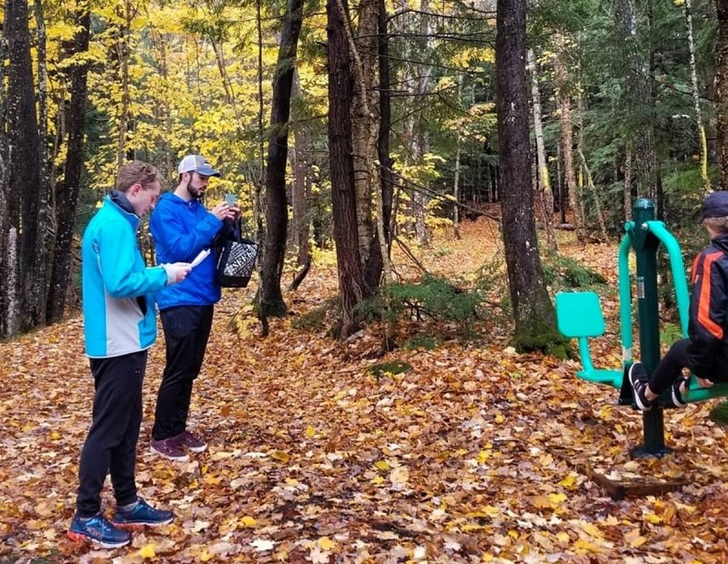 Two people filming another person on a fitness machine in the forest.