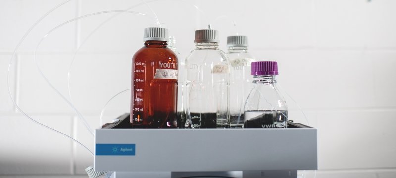 Four bottles of different shapes and sizes that all have liquid measurement marks on their sides sit in a tray.