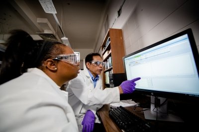 A researcher points at a computer screen while another researcher looks on.