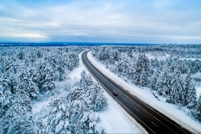 Aerial view of a car drining on a road through a snow-covered forest.