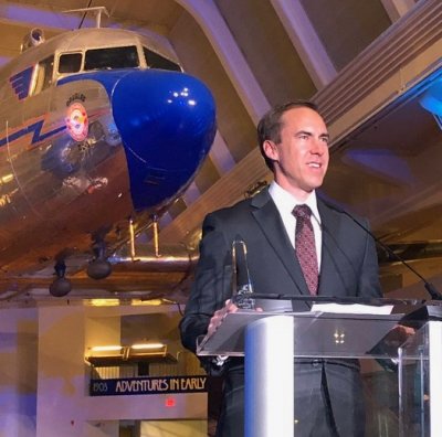 Brad King at a podium with an airplane in the background.