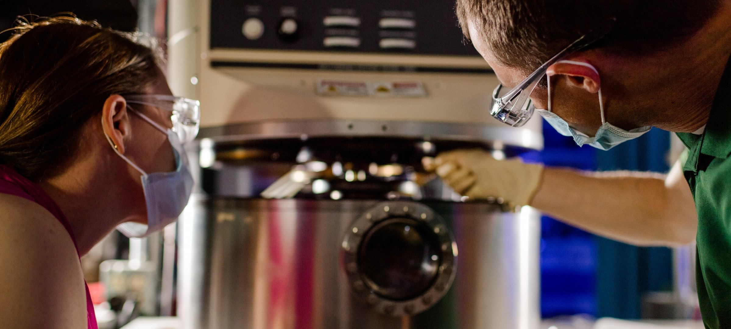 Two researchers with goggles removing a sample inside the lab.