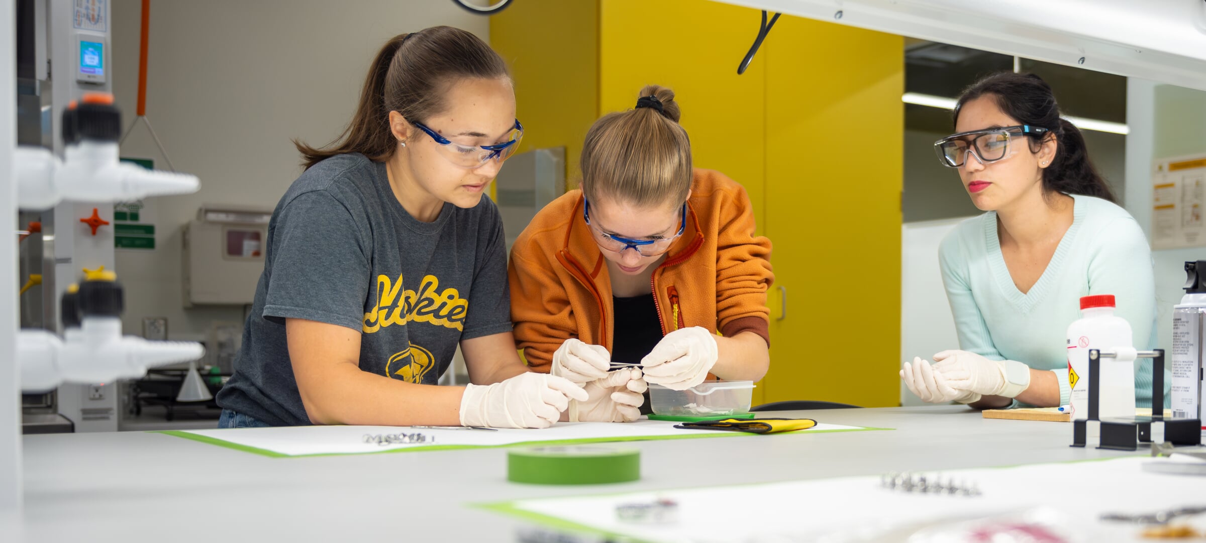 Three students with gloves working on a small object