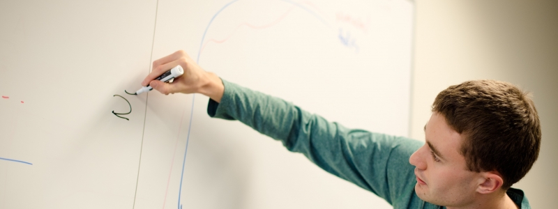 Student writing on a whiteboard, drawing a graph