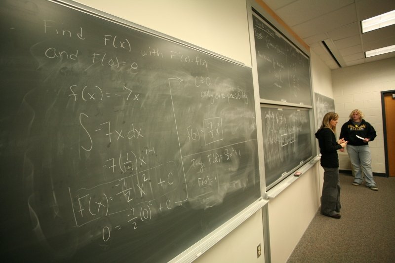 Faculty engaging students in front of a chalk board