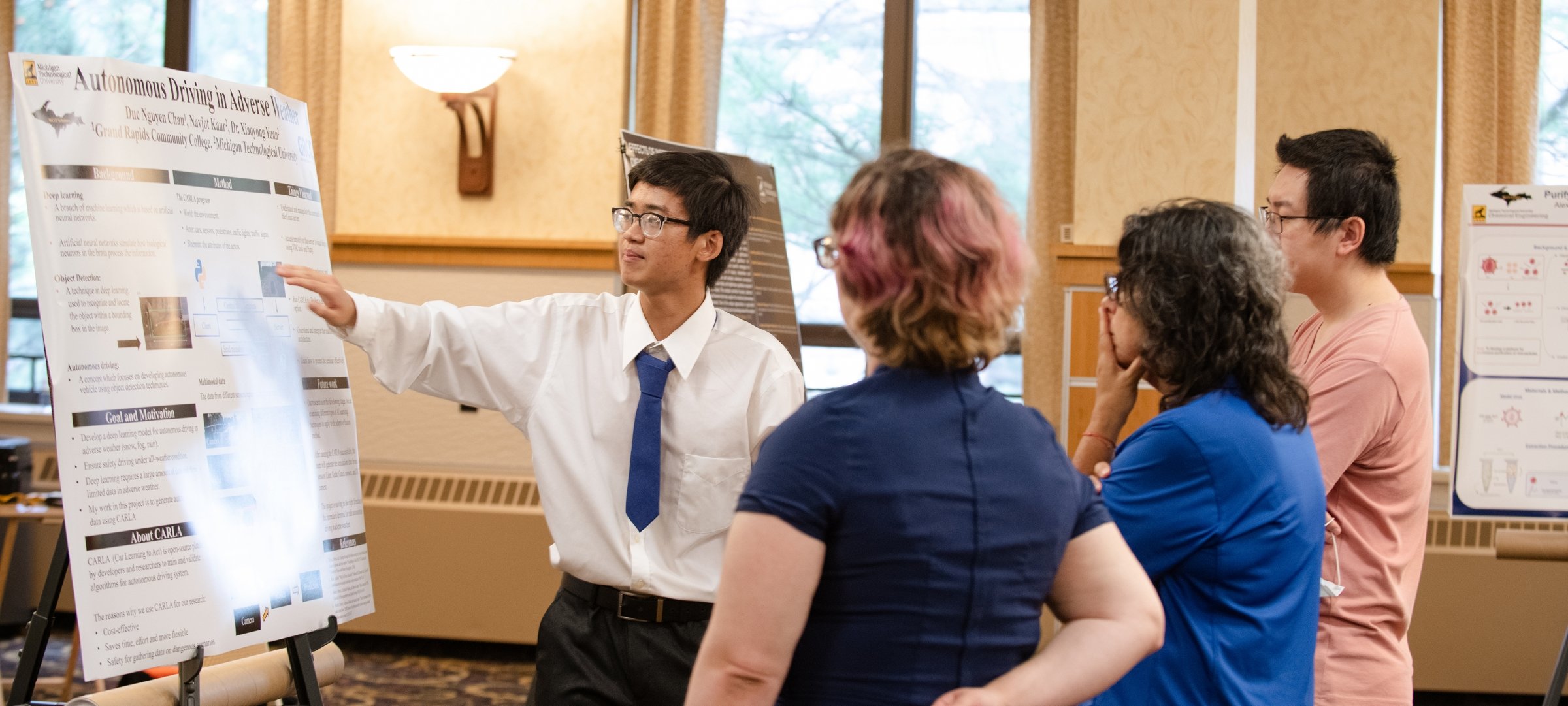 A student presents a research poster to three onlookers.