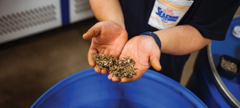 Hands holding trash confetti over a blue barrel.
