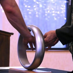 An engineer places their hand through a steel ring to receive the Order of the Engineer.