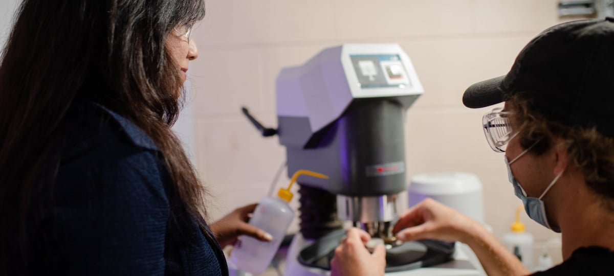 Trisha Sain with a wash bottle guiding a grad student putting a sample on a microscope.