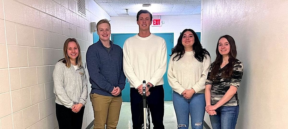 Five students stand by their project in the hallway.