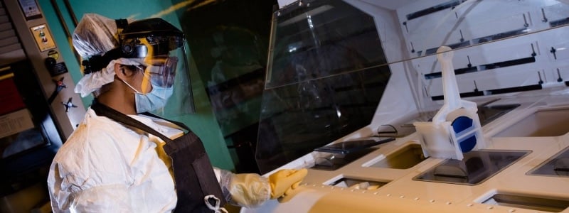 Researcher in full protective gear with an apron waiting for results next to a research area.