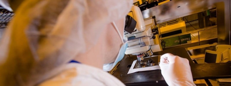 Researcher looking through a microscope in full protective lab gear.