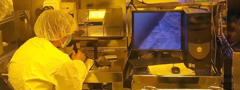 Researcher working at a station looking through a microscope in full protective lab gear.