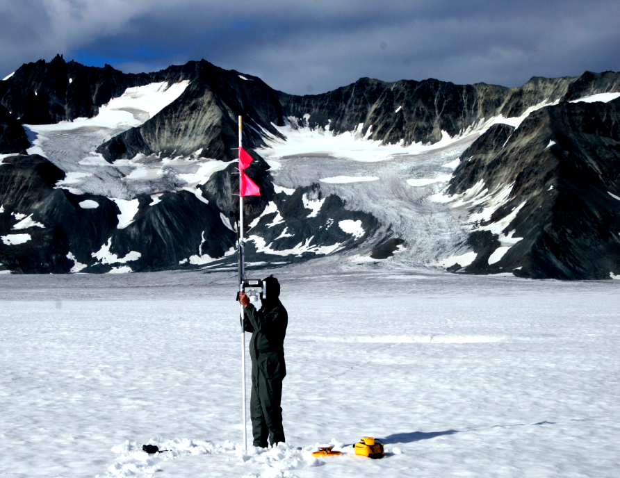 Person in the snow holding a meter with a flag on top.