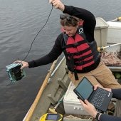 Researcher lowering equipment into the water from a boat.