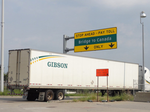 Semi truck passing under Bridge to Canada sign.