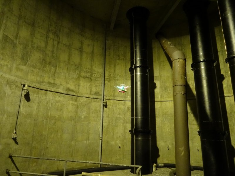 Drone flying in a room with pipes.