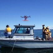 People on a boat with a hexacopter flying above.