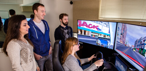 Three students watching another studnet test a driving simulator.