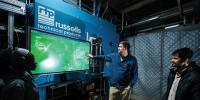 Students gathered around a professor pointing at a large screen with the russells technical products logo above it.