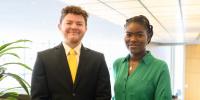 Two students speaking at spring commencement at Michigan Tech smile on a balcony overlooking the library.