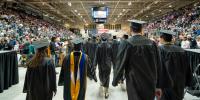 Students in caps and gowns walking into the commencement ceremony in the ice arena.