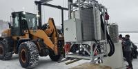 Front-end loader lifting the power station on a snowy day.